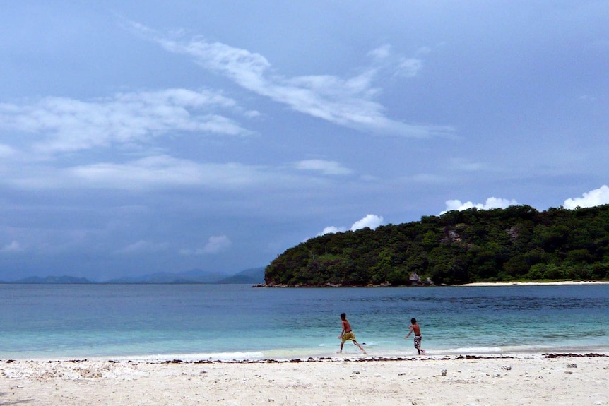 Two children play on a white sandy beach with bright blue water in Lombok.