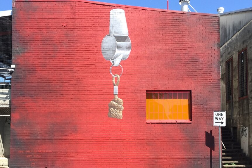 A mural on a red brick wall of a large silver whistle