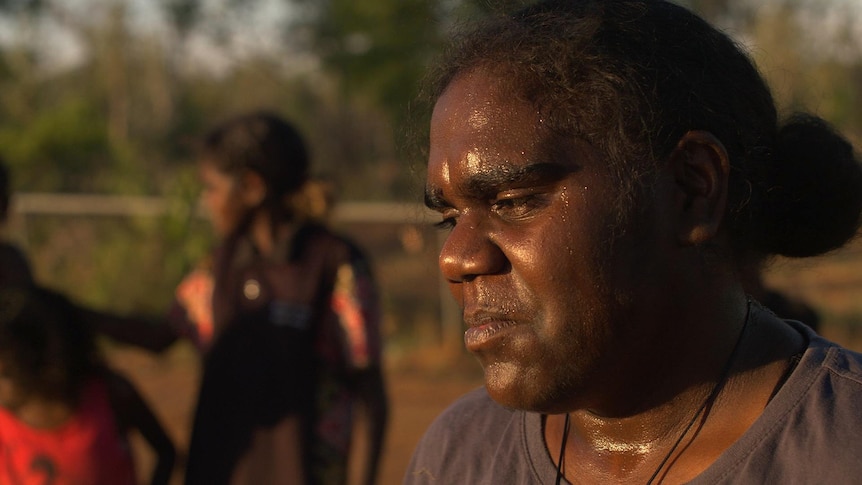 A young woman looks to the side, a sad expression on her face. Her face is sweaty from the summer heat.