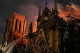 Firefighters spray water onto a burning cathedral as embers drift across a dark sky