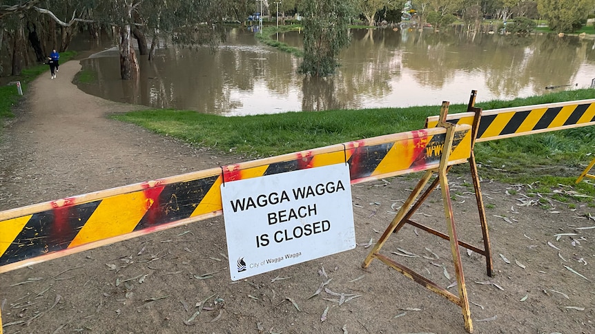 A sign saying Wagga Beach is closed near a large body of water.
