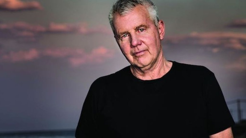 A man with short hair and a black shirt faces the camera 