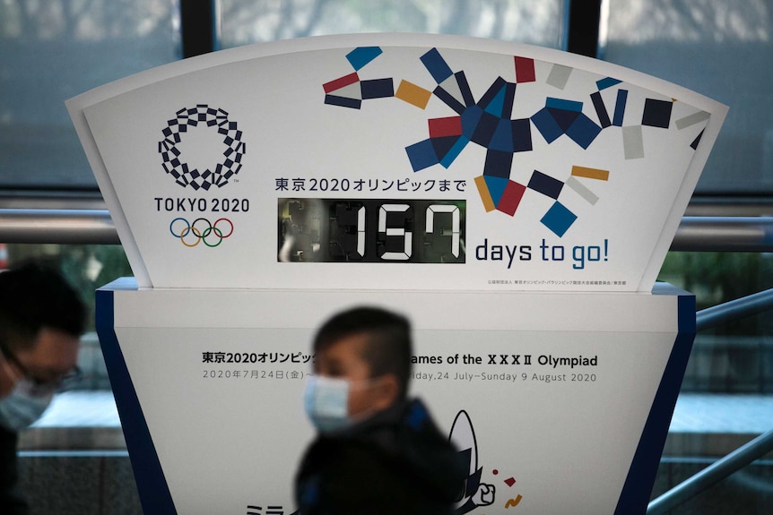 A countdown clock shows 157 days to the Tokyo Olympics, as people wear masks to avoid coronavirus.