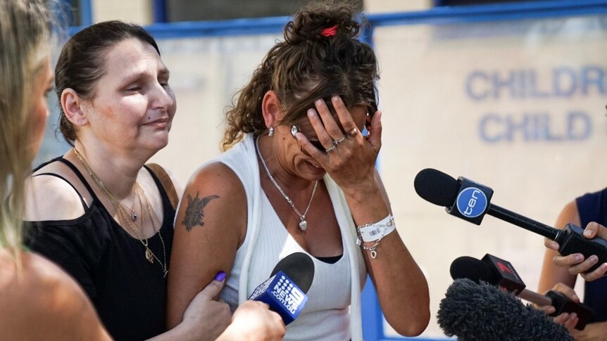 A distraught Lacey Harrison holds her head in her hand as she speaks to reporters outside PMH.