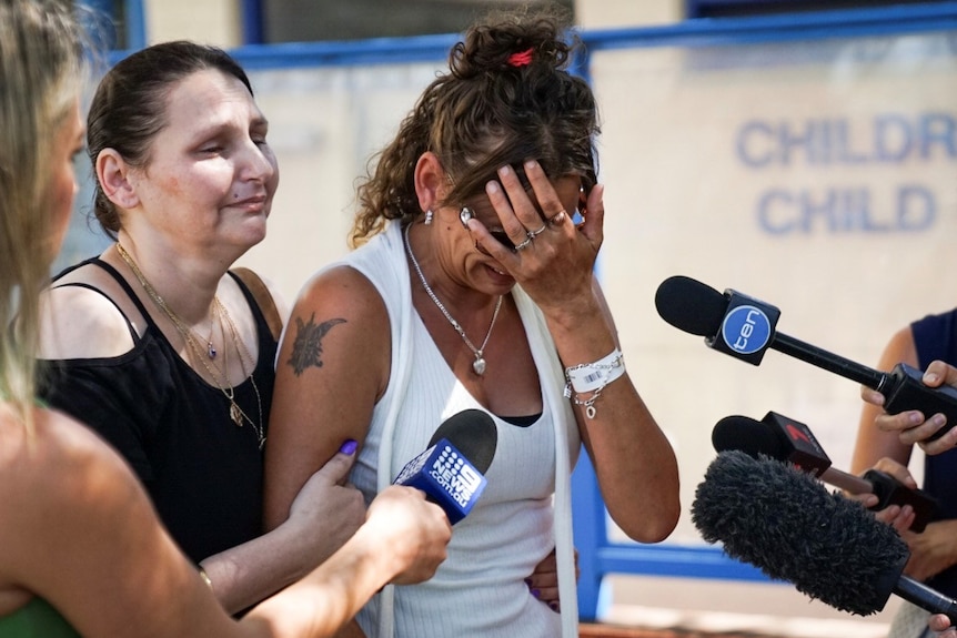 A distraught Lacey Harrison holds her head in her hand as she speaks to reporters outside PMH.