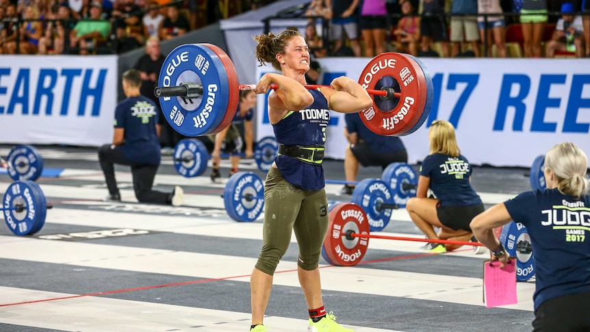 A woman lifting heavy weights in a big hall with people watching on