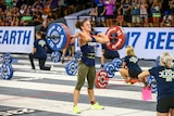 A woman lifting heavy weights in a big hall with people watching on