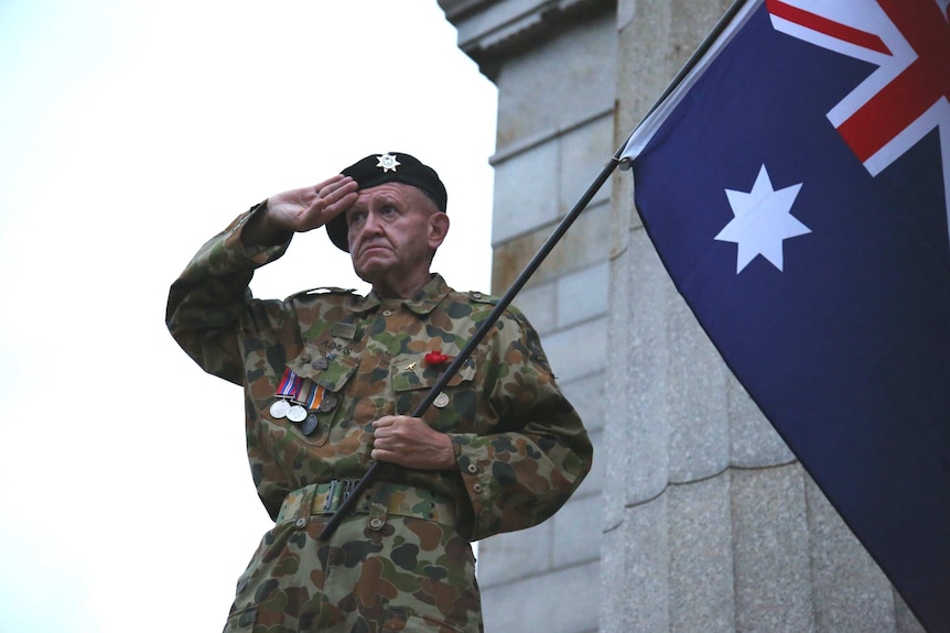 Corporal A. Davis, at Melbourne's Anzac Day dawn service, salutes as he holds the Australian flag.