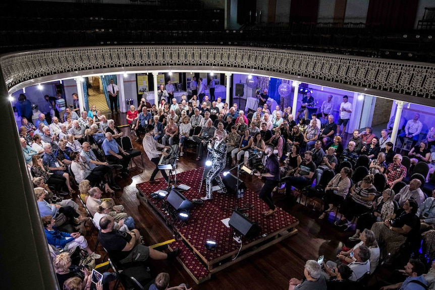 A band playing in an old town hall to a large crowd.