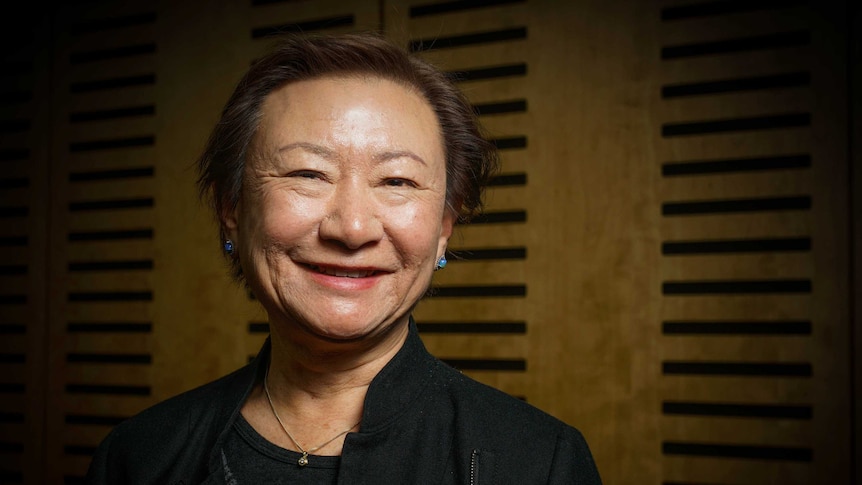 A smiling older woman of Asian descent photographed in a dark room.