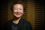 A smiling older woman of Asian descent photographed in a dark room.