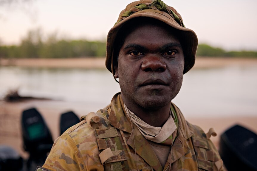 a close-up of an aboriginal man in army uniform looking at camera