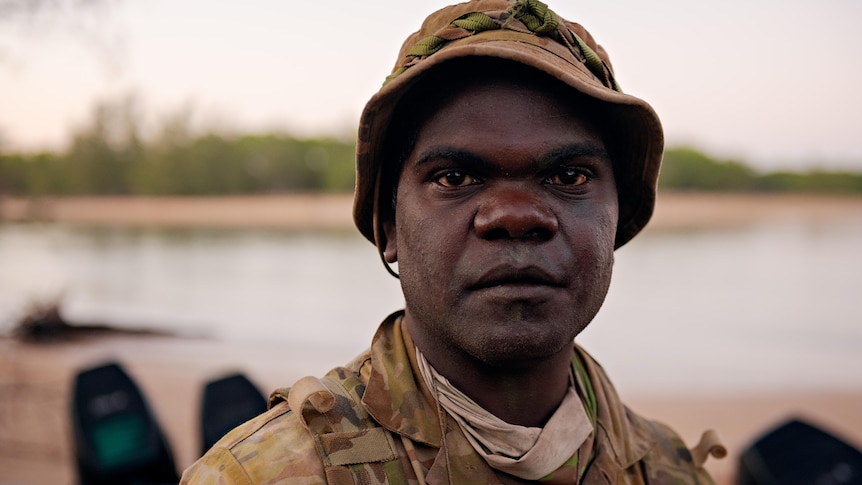 a close-up of an aboriginal man in army uniform looking at camera