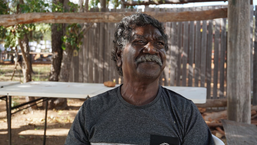 Murphy Yunupingu sits smiling in a grey shirt in the shade