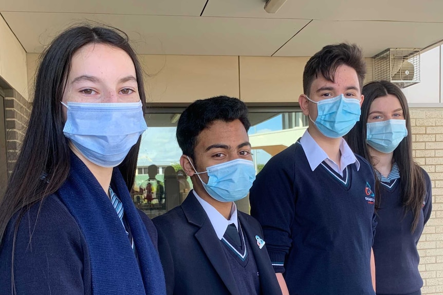 Two female and two male high school students wearing blue masks stand in a line.