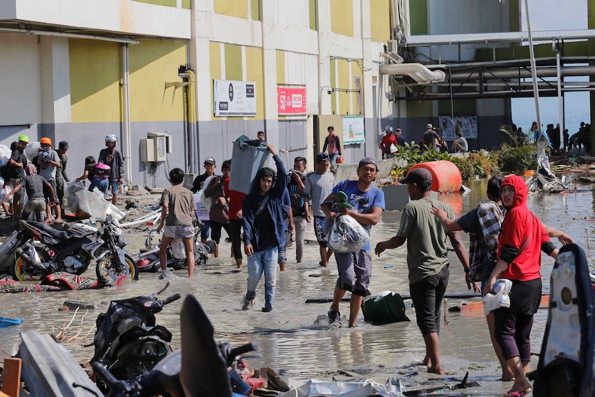 People are and carrying goods and scrambling through flooded road.