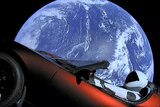 A view shows a Tesla Roadster in space with Earth in the background.