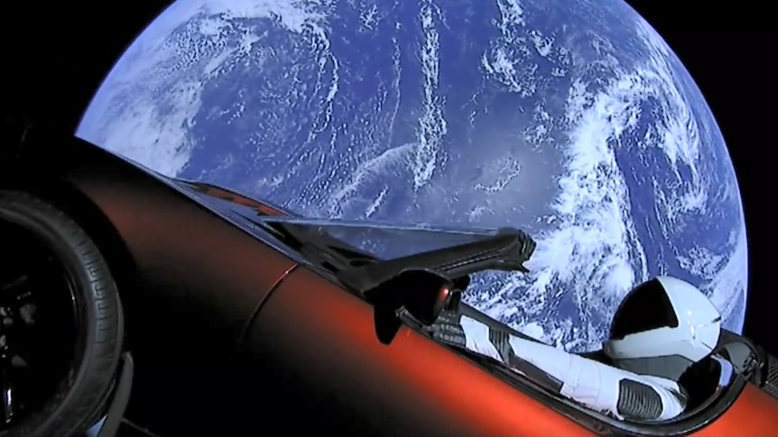 A view shows a Tesla Roadster in space with Earth in the background.