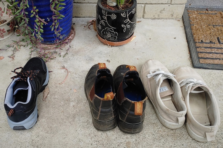 Three pairs of shoes lined up near a door mat. One shoe is missing.