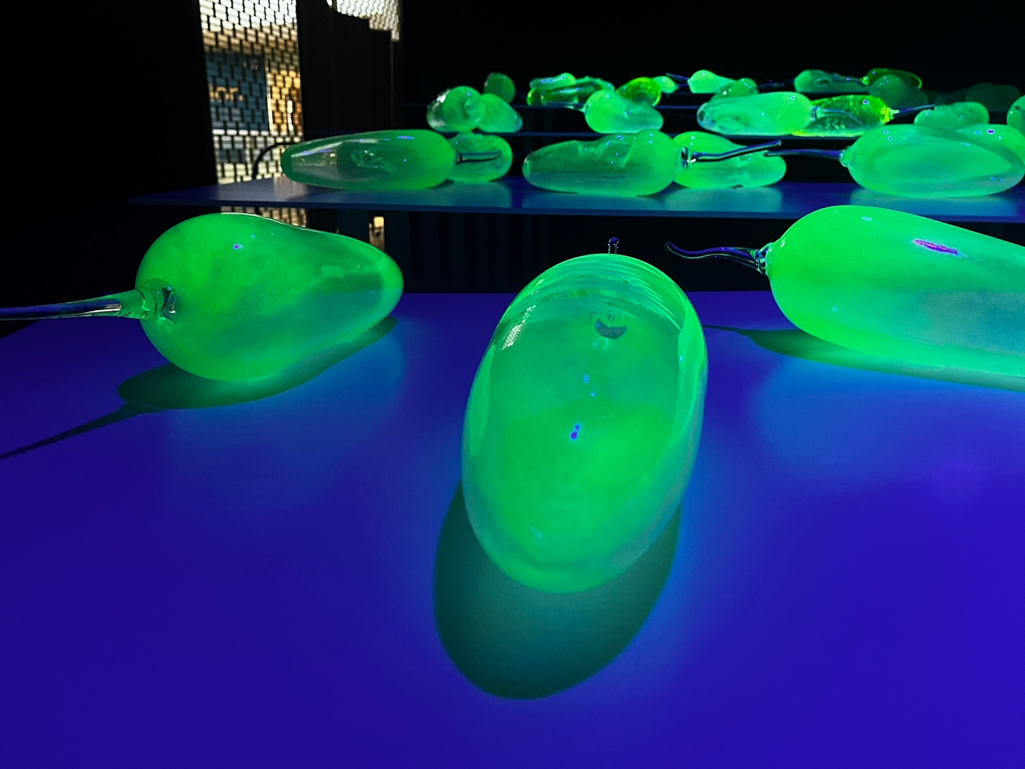 Greenish-yellow glass fruits glow on a blue table in a dark room