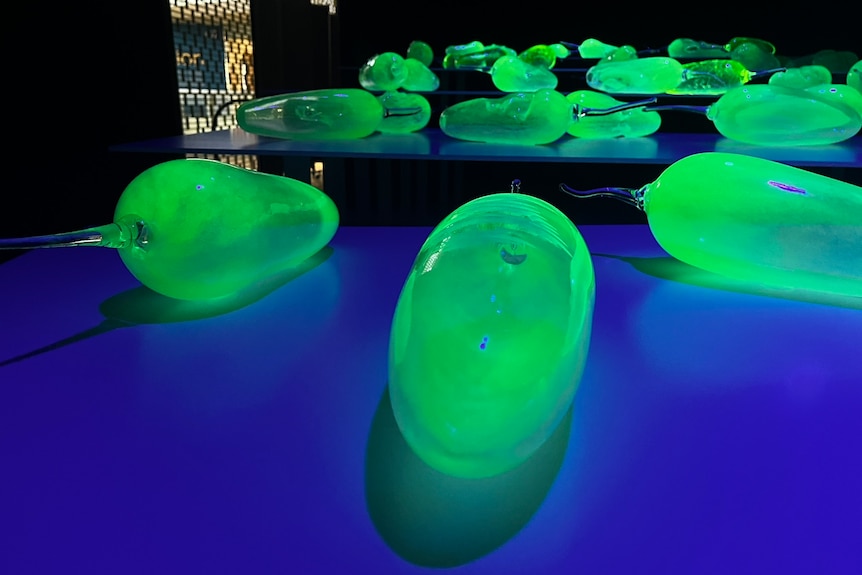 Greenish-yellow glass fruits glow on a blue table in a dark room