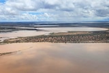 An aerial shot of a mass of reddish-brown water in an outback landscape.