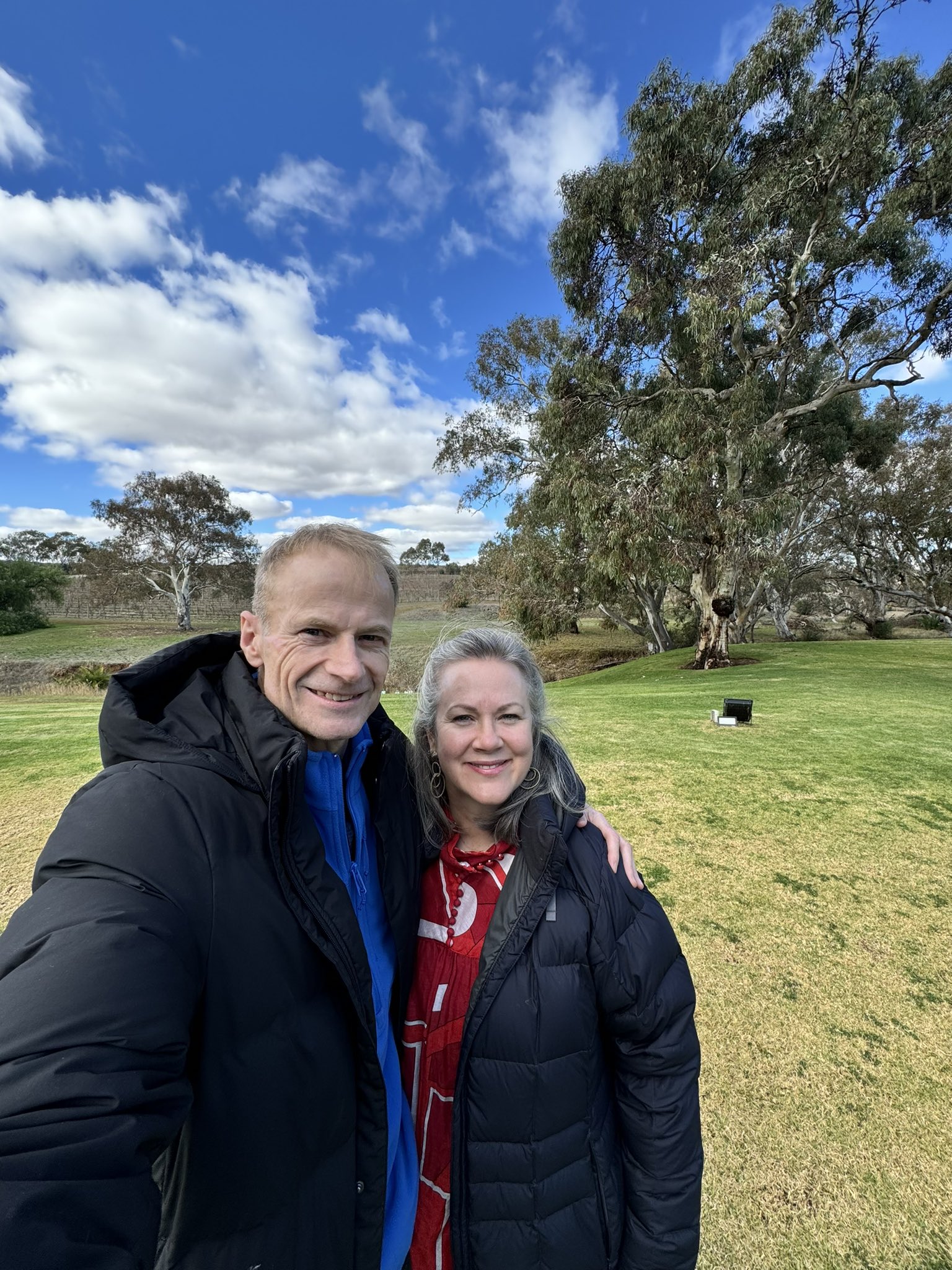     Richard Scolyer y su esposa, la Dra. Katie Nicoll, tomándose una selfie con hierba verde y cielo azul de fondo