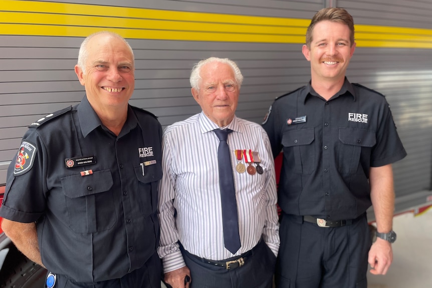 Three smiling men, older in dark grey uniform, elderly, grey hair, in light shirt, dark tie, medals, youngest in uniform.