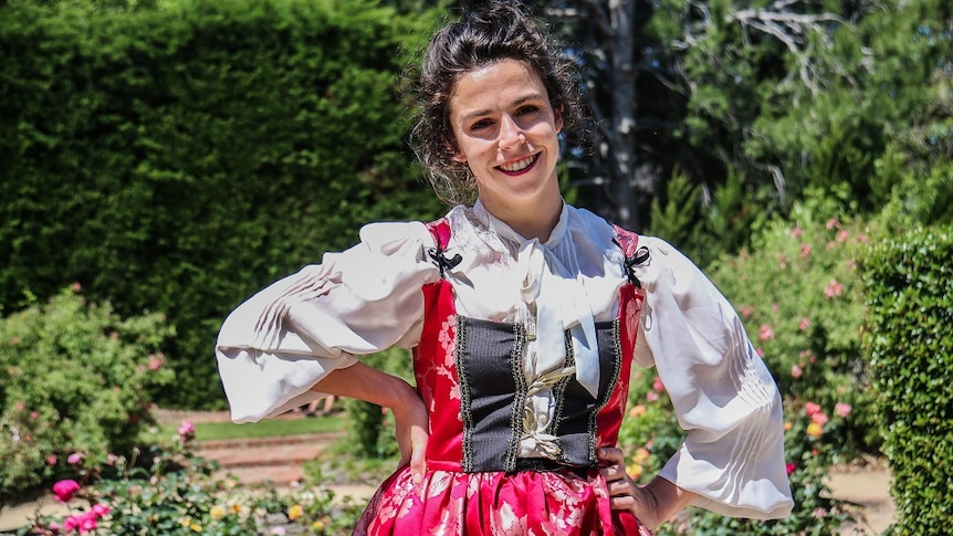 An actress wears a Shakespearean dress in St Kilda Botanical Gardens on a sunny day.