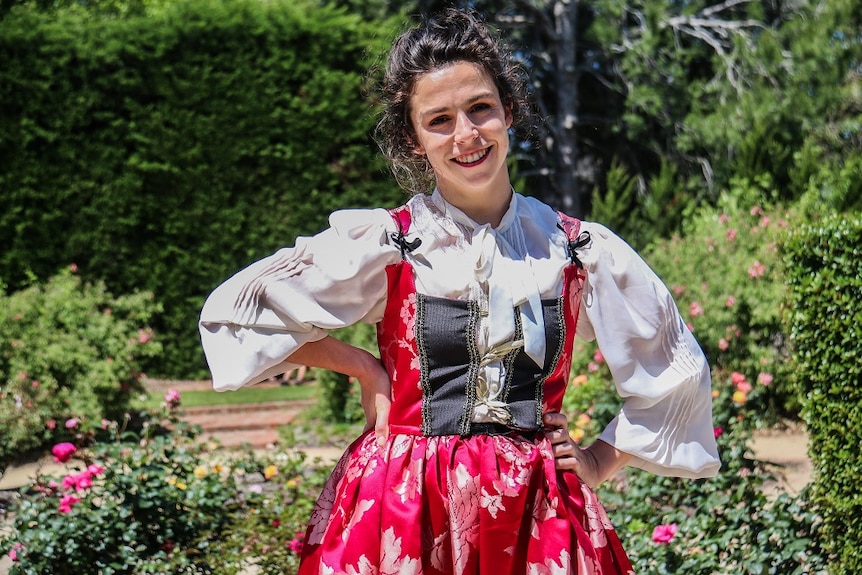 An actress wears a Shakespearean dress in St Kilda Botanical Gardens on a sunny day.