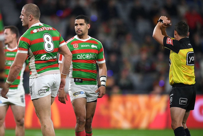 A rugby league player with his back turned as a referee crosses his arms in the air.