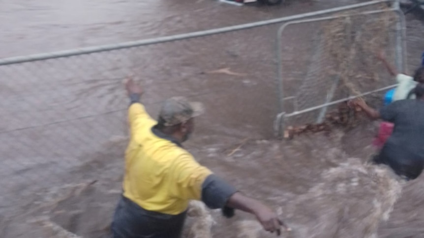 Several people wading through dark brown floodwaters