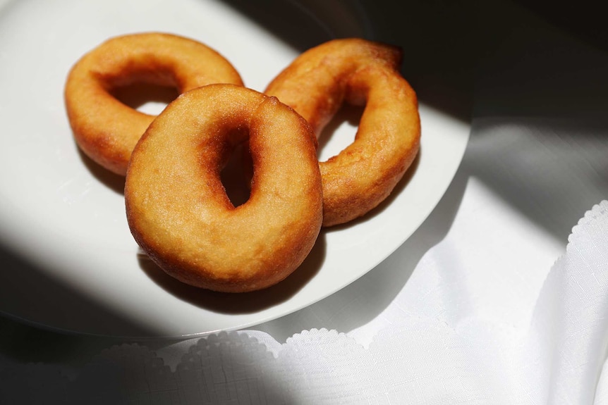 A close up of three freshly made Grispelle, doughnuts that originated in southern Italy, still made in Australia.