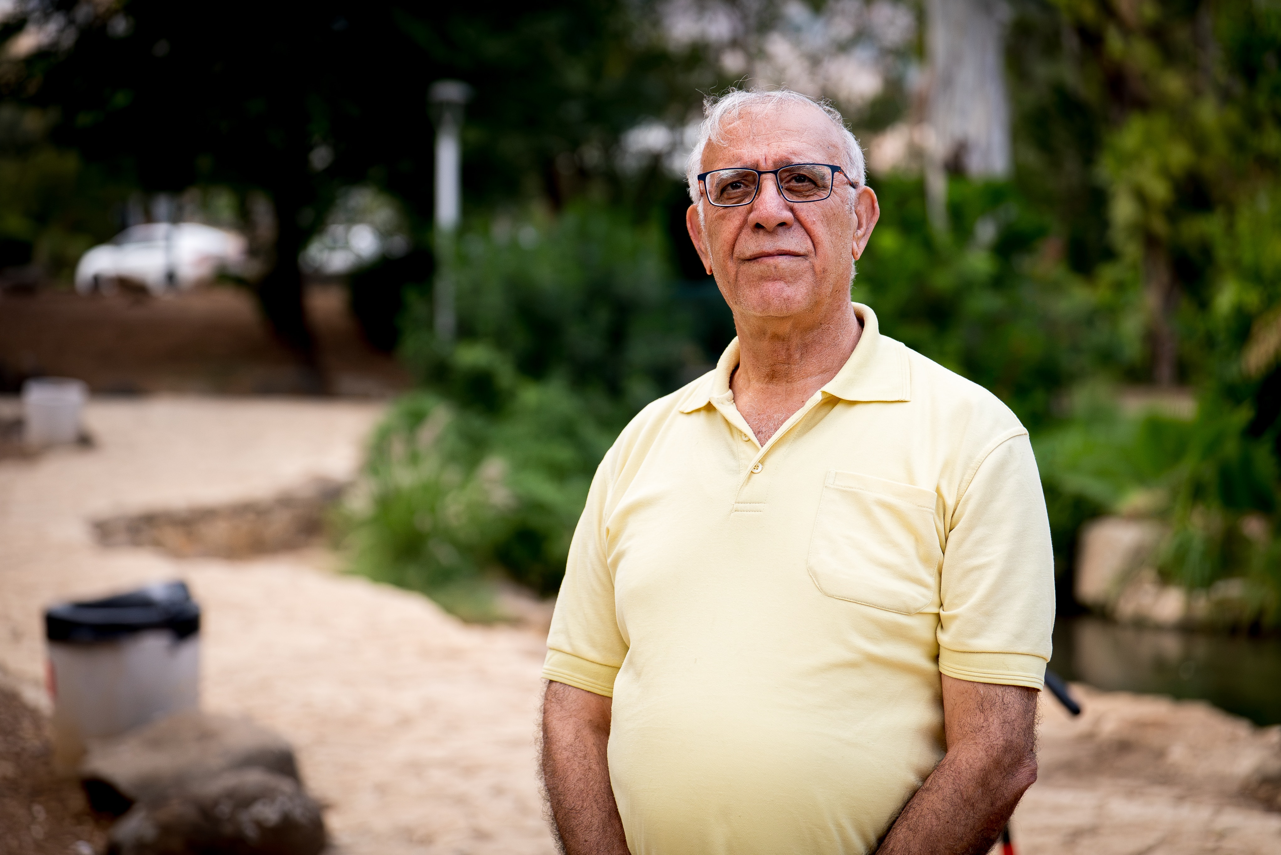 Herzl Ben Asher, an Israeli man wearing a yellow shirt and glasses, sits.