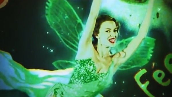 A smiling woman dressed as a green fairy, complete with green wings