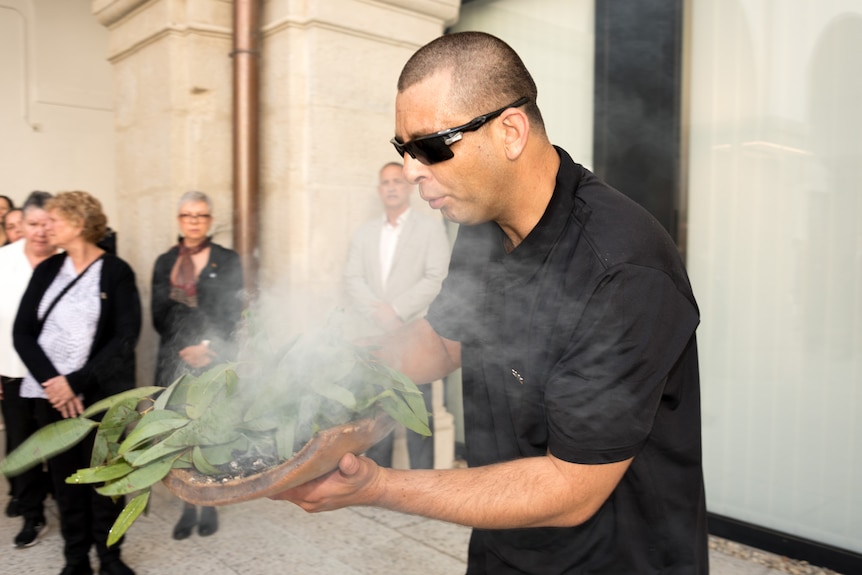 an Aboriginal man does a smoking ceremony with eucalyptus leaves