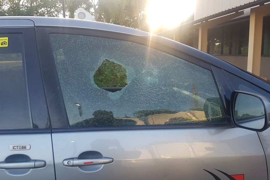 A silver taxi with a large hole in the smashed driver's side window 