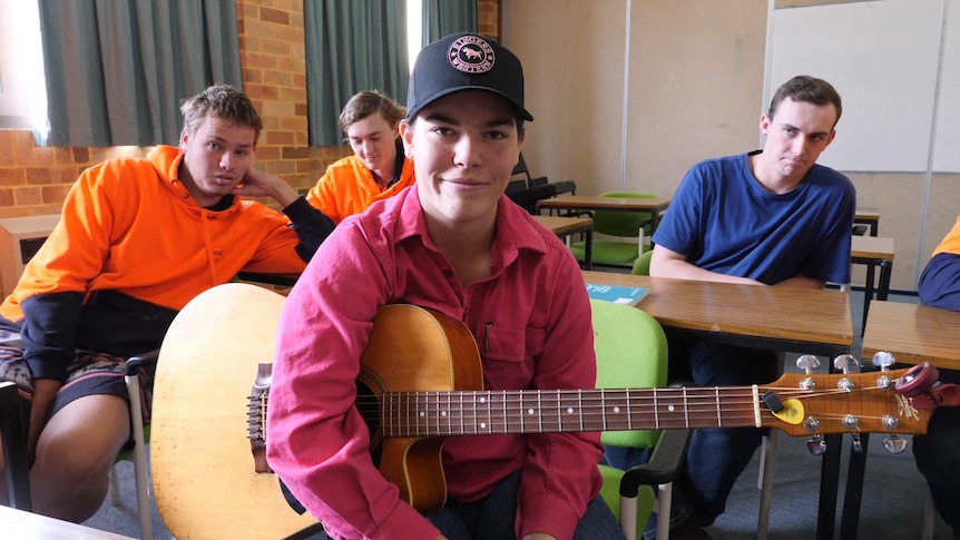 A young woman in a pink shirt and cap holding a guitar with three young men in background