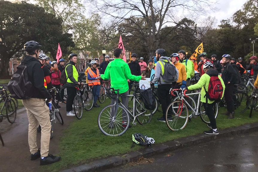 Protesters wearing high-vis and on bikes standing on grass in Carlton Gardens in the early morning.