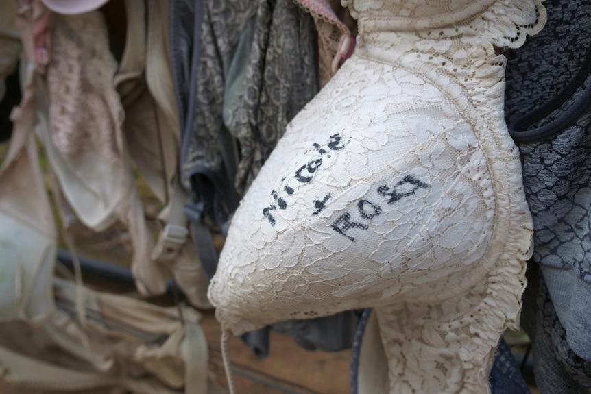 A close-up of a white lace bra with the names Nicole and Rosa written on a bowl in black permanent ink.