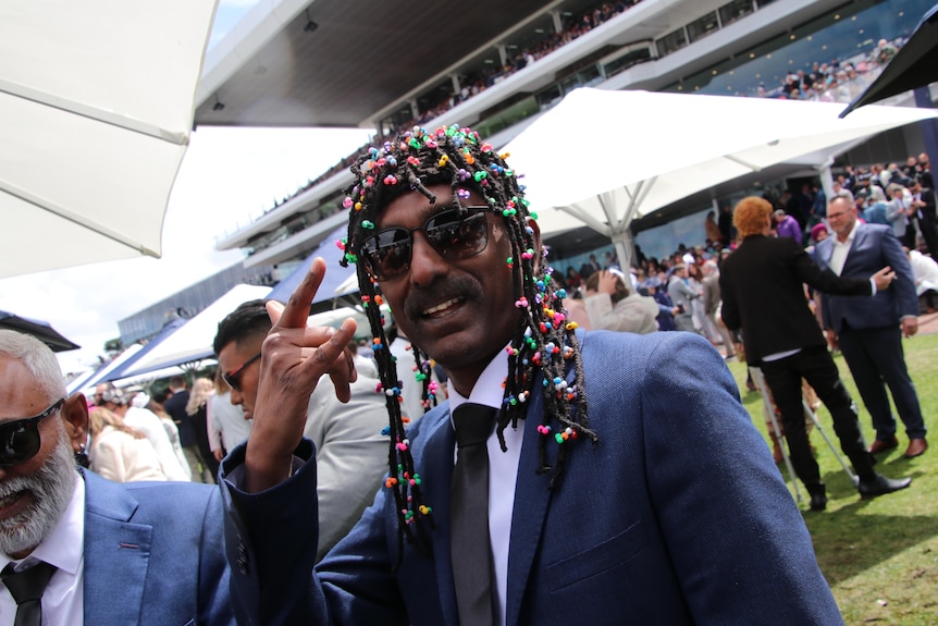 A man at the Melbourne Cup wearing braids and a suit.