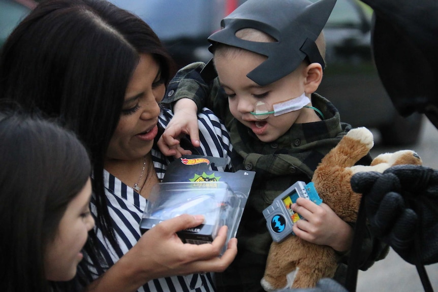 Eli Vale, being held by his mother, receives a bag of presents from Batman