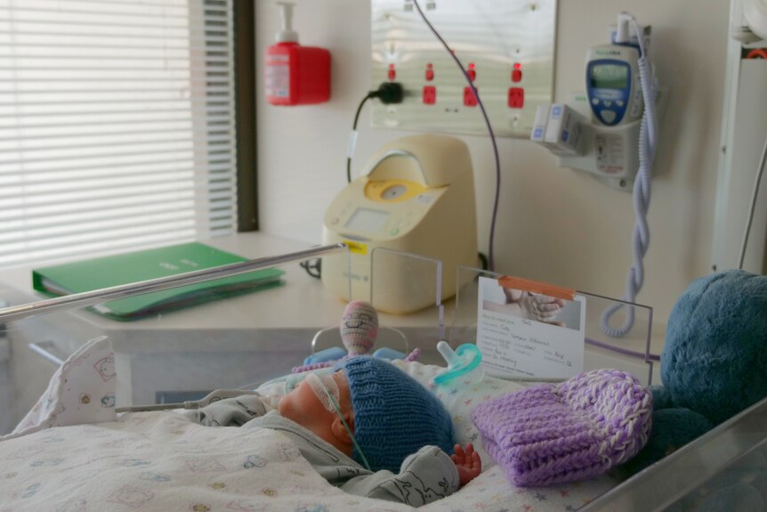 Baby tide lying in crib next to the window, tubes on his face.