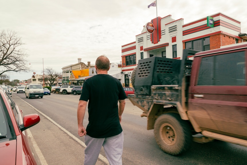 A man walks on a country street with his back to the camera, and a pub in the background.