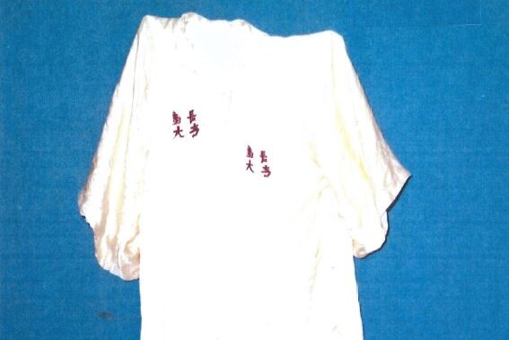 A white silky kimono with small red oriental markings lies on a blue surface.