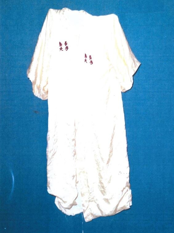 A white silky kimono with small red oriental markings lies on a blue surface.