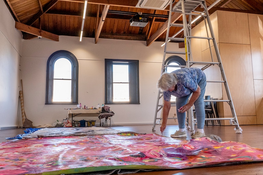 A woman paints on the ground in a warehouse space.