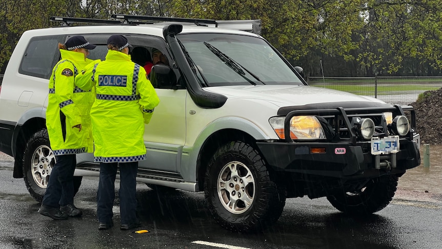 Two police officers in hi-vis jackets speak to a man in a four-wheel drive.