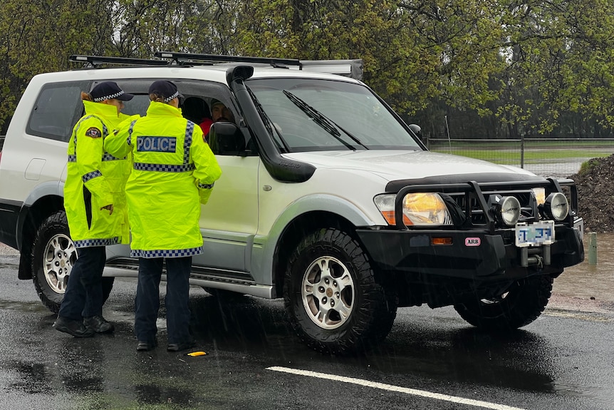 Two police officers in hi-vis jackets speak to a man in a four-wheel drive.