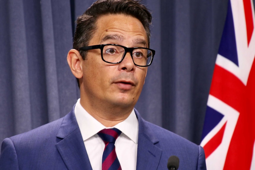 WA Treasurer, Ben Wyatt standing beside flag